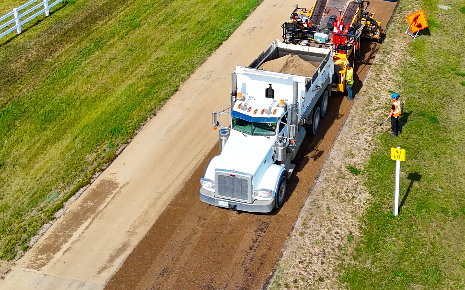 Compacted gravel base of an acreage driveway with the dump truck feeding the paver