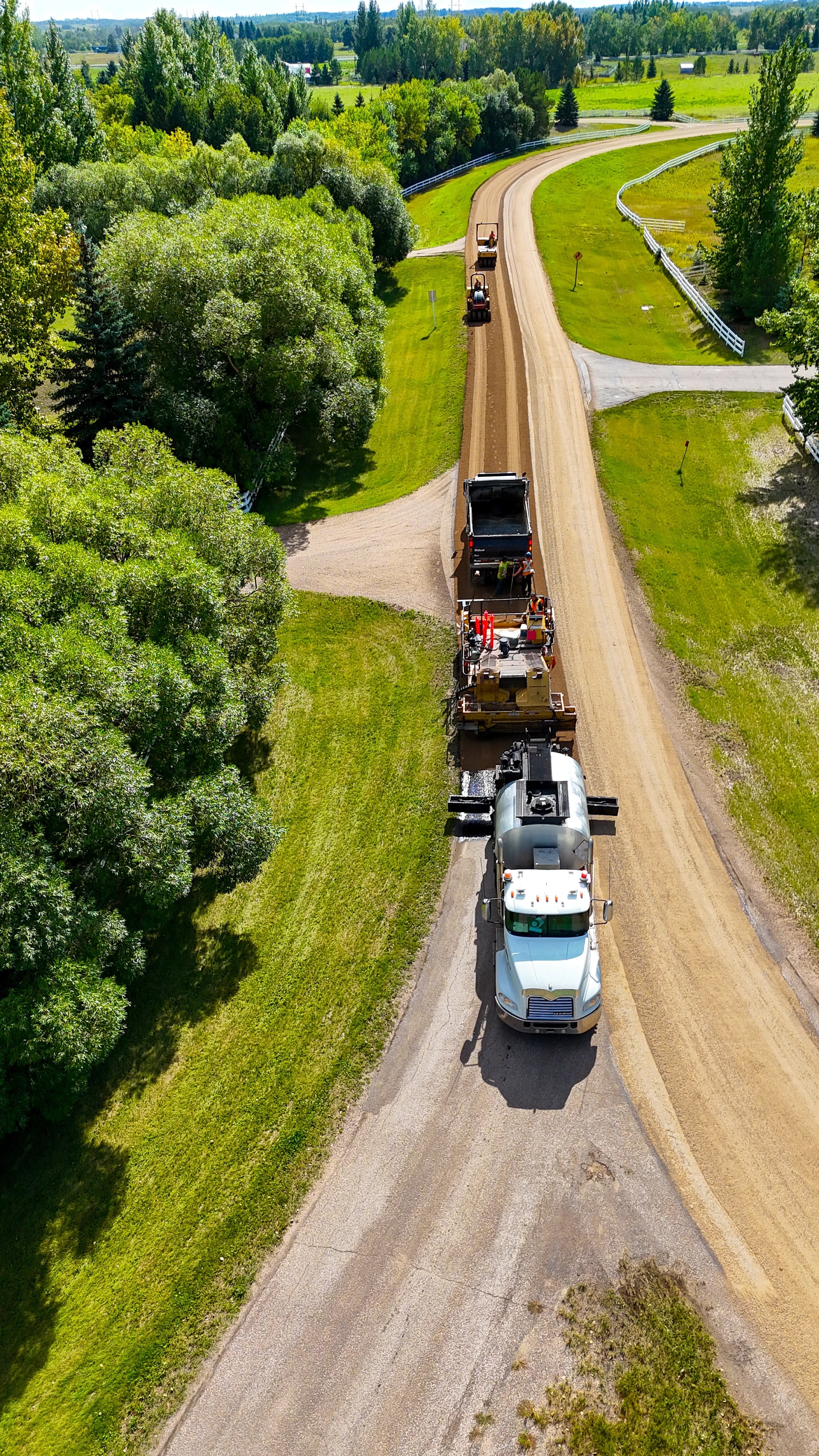 Chip seal crew rolling a new wearing surface on a country road beside a stand of trees
